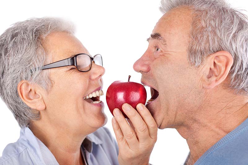 Пара в возрасте кусает яблоко здоровыми и красивыми зубами
