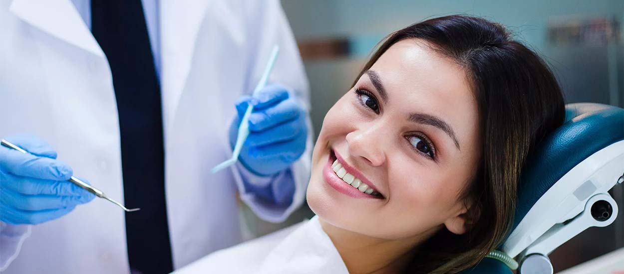 Девушка сидит в стоматологическом кресле перед осмотром специалиста и улыбается